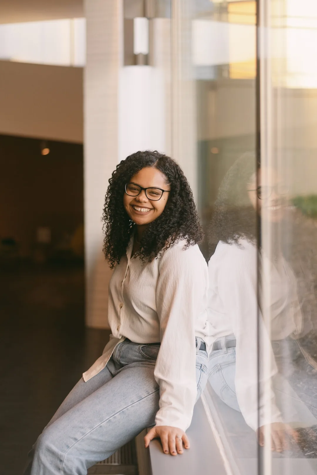 Nicole Olaniyi leaning against a glass wall in a university atrium, smiling.