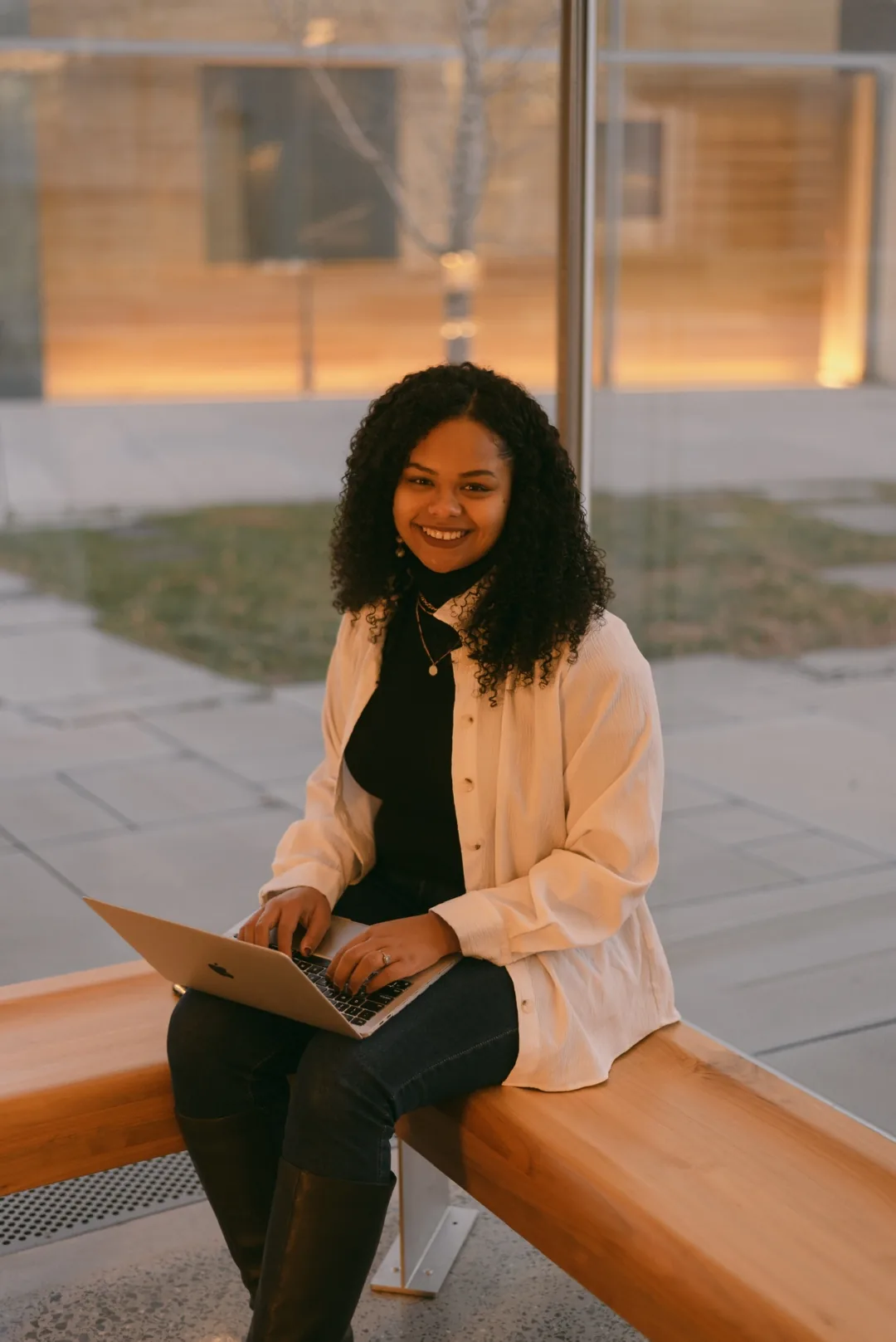 Nicole Olaniyi, founder of Lionheart Coaching Academy, seated with a laptop outside a university building at golden hour.